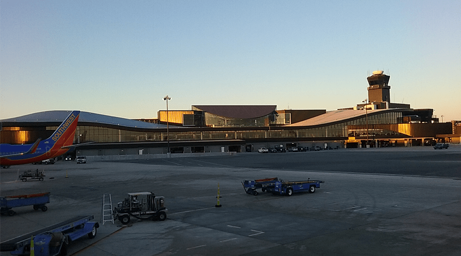 Modern airport building with golden glass façade and control tower, bathed in early morning light. Southwest Airlines plane parked nearby.