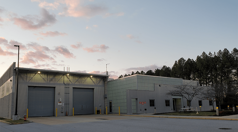 Modern facility at dusk with loading bays, a glass-paneled section, and surrounding trees, highlighting industrial architecture and operational readiness.
